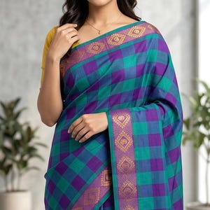 May include: A saree featuring a purple and teal checkered pattern with a wide border in purple and gold, decorated with repeating geometric and floral motifs. The garment is paired with a solid mustard yellow blouse and includes the text Satya Fashions.