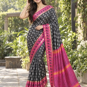 May include: A charcoal gray saree featuring a repeating white leaf pattern, accented by a wide, vibrant magenta border with gold trim and black paisley motifs. The garment includes a matching magenta pallu with intricate black line-art designs.