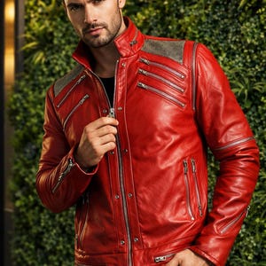 May include: A vibrant red leather jacket with multiple silver zippers and a textured gray shoulder panel. The jacket has a classic collar and a tailored fit. The model is wearing a black shirt and black pants.