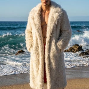 Peut inclure: Un long manteau en fausse fourrure crème avec un large col. Le manteau est porté ouvert, révélant un short rouge. L'arrière-plan présente une plage avec des vagues océaniques et un ciel bleu clair.