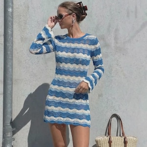 May include: A blue and white striped, long-sleeved mini dress. The dress has a wavy pattern and is paired with a woven tote bag with brown leather handles. The dress is made of a lightweight material, perfect for warm weather.