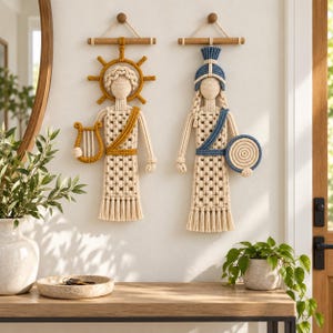 May include: Two macrame wall hangings featuring stylized figures. The left figure has a yellow sun halo and a lyre. The right figure wears a blue helmet and holds a circular shield. Both are crafted from cream-colored cord on wooden dowels.