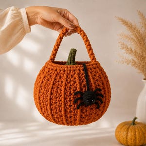 May include: A round, orange crocheted pumpkin basket featuring a textured ribbed design, a green crocheted stem at the top, and a single handle. A small, black crocheted spider with eight legs and two eyes is attached to the side of the pumpkin.