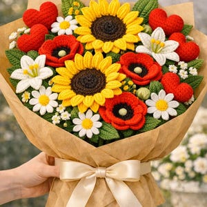 Puede incluir: Un ramo artesanal de flores de ganchillo, que incluye girasoles, amapolas, margaritas y lirios blancos, con acentos de corazón rojo. El ramo está envuelto en papel marrón y atado con una cinta de satén color crema.