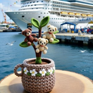 May include: A crocheted teddy bear plant pot with three small teddy bears on green leaves. The brown pot is decorated with white flowers and sits on a wooden surface. A cruise ship is in the background.