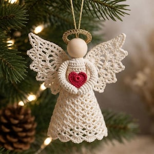 Può includere: Un angelo decorativo all'uncinetto in filato color bianco sporco con una testa in perla di legno liscia, un'aureola dorata e un piccolo cuore rosso cucito al centro del petto. L'angelo presenta ali in pizzo intricate e una gonna svasata.