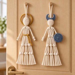 May include: Two macrame wall hangings made of off-white cotton rope. The left figure features a gold circular halo and a gold waist tie. The right figure features a blue crescent moon headpiece and a blue circular shield held at the side.