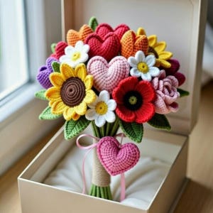 May include: A handmade crochet bouquet with a variety of flowers and hearts in a beige gift box. The bouquet includes sunflowers, daisies, and hearts in shades of red, yellow, orange, pink, and purple. The bouquet is tied with twine and a pink ribbon.