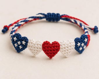 Op de afbeelding: Een armband met gehaakte harten in rood, wit en blauw. De blauwe harten hebben witte sterren, de andere zijn effen rood en wit. Het verstelbare koord is ook rood, wit en blauw. Een charmant, handgemaakt accessoire.