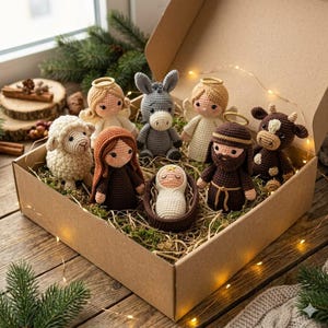 May include: A set of crocheted nativity figures inside a cardboard box, including a baby in a cradle, figures in brown robes, a white sheep, a gray donkey, a brown cow, and two angels with gold halos, all nestled on a bed of dried grass and lights.