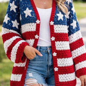 Op de afbeelding: Een gehaakt vest in rood, wit en blauw, met een ontwerp dat doet denken aan de Amerikaanse vlag. De blauwe delen hebben witte steraccenten, terwijl de mouwen rood-witte strepen vertonen. Het vest heeft bloemvormige knopen.