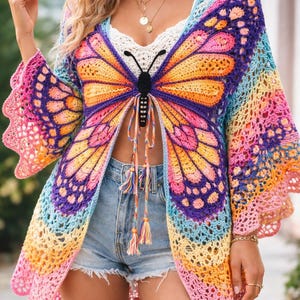 Puede incluir: Un cárdigan de mariposa de ganchillo de frente abierto y colorido. Las alas presentan un degradado de rosa, naranja, amarillo, azul y morado. El cárdigan tiene mangas largas con bordes festoneados y un cuerpo de mariposa negro con cierre de lazo.