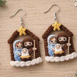 Könnte beinhalten: Ein Paar handgefertigte Häkelohrringe mit einer Krippenszene. Jeder Ohrring zeigt ein braunes Haus mit einem gelben Stern und darin eine Familie in Blau, Braun und Weiß. Ideal für Weihnachten.