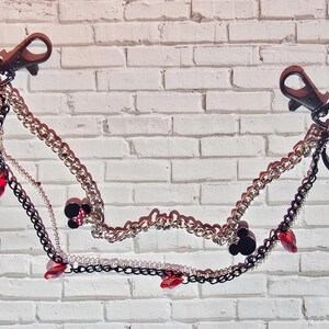 May include: A multi-strand decorative chain featuring two black lobster clasps at the ends. The design includes silver and black metal links, red crystal accents, and small charms depicting cartoon mouse characters in red, black, and yellow colors.