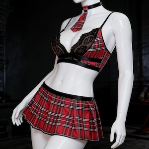 May include: A red and black plaid lingerie set featuring a bralette with black lace detailing, a matching pleated mini skirt, and a plaid tie. The set includes a black choker. The outfit is displayed on a mannequin.