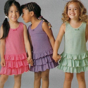 May include: Three girls wearing sleeveless dresses with ruffles. The dresses are pink, purple, and green. The girls are holding hands and smiling. The image is from a sewing pattern for children's clothing.