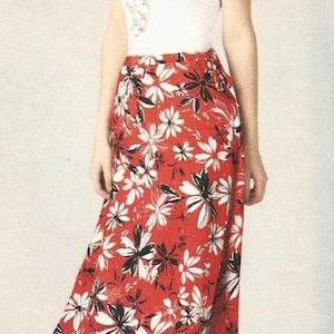 May include: A woman wearing a white top and a red skirt with a floral pattern. The skirt features white and black flowers on a red background. She is also wearing black sandals.