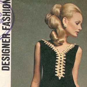 May include: Vintage Simplicity sewing pattern featuring two dress designs. One is a long, coral-colored dress with long sleeves and decorative trim. The other is a black dress with a decorative neckline. The pattern includes a "Designer Fashion" label.