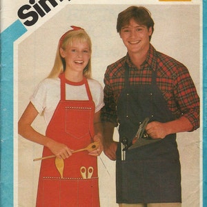 May include: Two people wearing aprons. The person on the left is wearing a red apron with pockets and a wooden spoon. The person on the right is wearing a black apron with pockets and is holding a hand plane.