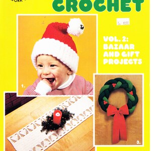 May include: A yellow book cover with the title "CHRISTMAS CROCHET" in green letters. The cover features a baby wearing a Santa hat, a crocheted table runner with a candle, and a crocheted wreath with a red bow. The book is titled "VOL. 2: BAZAAR AND GIFT PROJECTS."