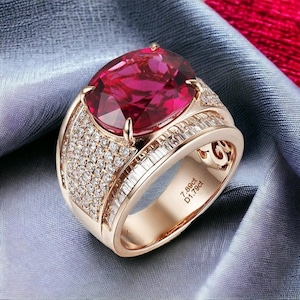 Op de afbeelding: Een roségouden ring met een grote, ovaal geslepen robijn. De ringband is bezet met kleine, ronde diamanten en baguette-geslepen diamanten. De ring heeft de tekst "7.89ct D1.79ct" gegraveerd aan de binnenkant van de band.
