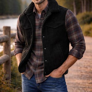 Könnte beinhalten: Eine schwarze Weste mit Sherpa-Kragen über einem karierten Hemd und blauen Jeans. Die Weste hat eine Knopfleiste und zwei Vordertaschen. Das karierte Hemd ist braun, rot und grau. Die Jeans sind mittelblau.