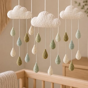May include: A handmade baby mobile featuring a crocheted sun and clouds. The clouds are white, and the raindrops are in shades of green, blue, and cream. The mobile hangs from a wooden ring, creating a whimsical nursery decoration.