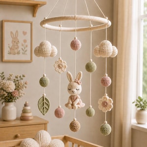 May include: A handcrafted baby mobile with a crochet bunny, clouds, flowers, leaves, and spheres in gentle pastel shades. The mobile is suspended from a wooden ring, perfect for a nursery.