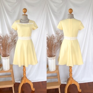 May include: A yellow dress with a white lace trim around the neckline and waist. The dress has short sleeves and a flared skirt.