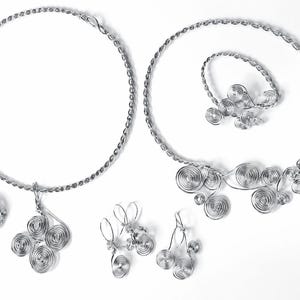 May include: A silver-toned jewelry set featuring a necklace, bracelet, earrings, and a ring. The necklace and bracelet have a twisted rope design. The earrings, ring, and necklace pendant feature spiral wire designs. The jewelry is displayed on a white background.