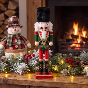 May include: A wooden nutcracker soldier wearing a tall black fur hat, a green jacket with gold trim, and red trousers, holding a small green drum. Beside it stands a plush snowman wearing a plaid hat and scarf, surrounded by pine branches.