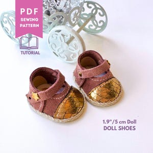 Op de afbeelding: Een paar poppenschoenen van 5 cm, voorzien van een mauve suède bovenwerk met een metallic gouden, getextureerde neus, een bandje met een kleine stervormige stud en een gevlochten rand. Inclusief een PDF-naaipatroon en handleiding voor de schoenen.