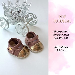 May include: A pair of miniature brown and gold doll shoes, 5 cm long, with a star detail, next to a decorative glass carriage. The shoes are designed for a 22 cm doll. The image includes the text "PDF TUTORIAL".