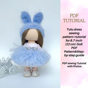 May include: A fabric doll with brown hair wearing a fuzzy blue bunny-ear hat and a light blue tulle tutu dress. The doll wears light pink shoes with flower accents. Text reads: PDF TUTORIAL Tutu dress sewing pattern+tutorial for 8.7-inch (22 cm) Doll.