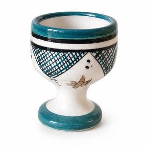 Puede incluir: Un huevero de cerámica con base blanca y borde y base turquesa. La taza presenta un patrón geométrico turquesa y negro alrededor del centro y un diseño floral. El huevero mide aproximadamente 7,6 cm de alto.
