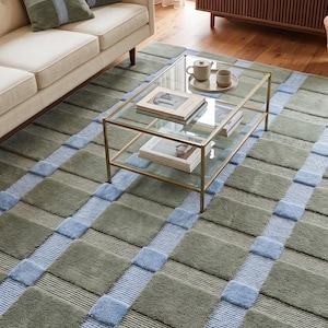 Pode incluir: Tapete estampado verde e azul com design geométrico. O tapete apresenta quadrados e listras alternados verdes e azuis. Uma mesa de centro de vidro está sobre o tapete.