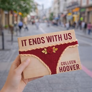 Könnte beinhalten: Holzbuchcover mit dem Titel "IT ENDS WITH US" und dem Autor "COLLEEN HOOVER". Es zeigt ein burgunderrotes Häkeldesign von Unterwäsche mit einer Rose und Blättern. Der Hintergrund ist eine verschwommene Stadtstraße.