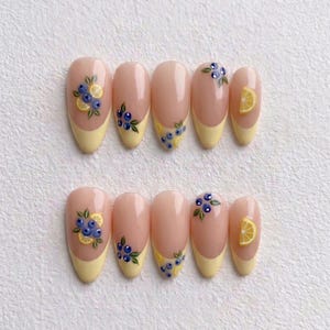 Puede incluir: Un conjunto de diez uñas artificiales con base rosa claro y puntas amarillas. Cada uña presenta un diseño de arándanos, rodajas de limón y hojas verdes. Las uñas son de forma ovalada y están dispuestas en dos filas de cinco.