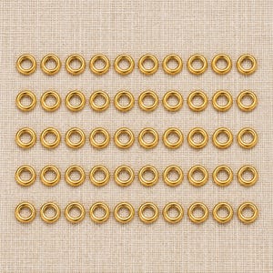 Gold-tone stainless steel closed jump rings. Pack flat lay; quantity check pending. 4mm outer diameter; 1.2mm wire. Buyer pack: 50 pieces.