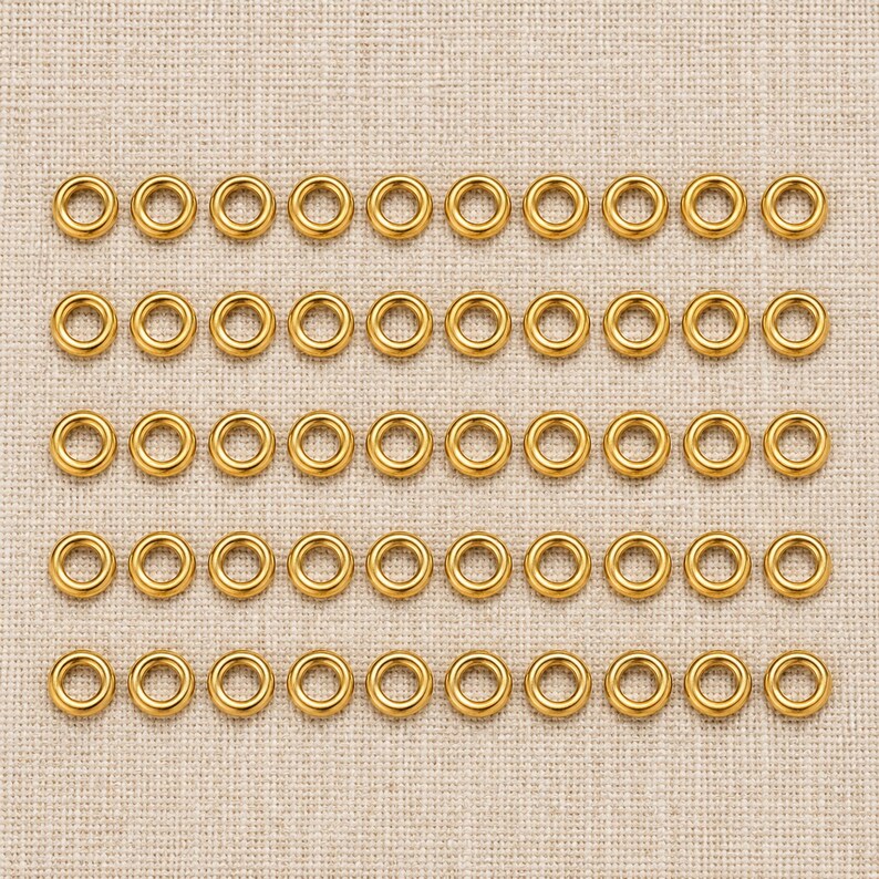 Gold-tone stainless steel closed jump rings. Pack flat lay; quantity check pending. 4mm outer diameter; 1.2mm wire. Buyer pack: 50 pieces.