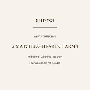 K&ouml;nnte beinhalten: Eine Produktinformationskarte mit dem Text aureza, WHAT YOU RECEIVE, 2 MATCHING HEART CHARMS, Red centre, Gold tone, No chain und Styling props are not included. Der Hintergrund ist ein einfarbiger, heller Cremeton mit dunkelbraunem Text.