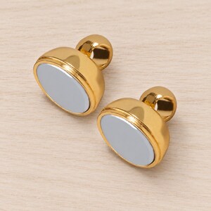 Two matching gold-tone domed magnetic clasp halves on natural linen, showing their original silver-grey contact faces and both attachment eyes; representative sample from five complete sets supplied.