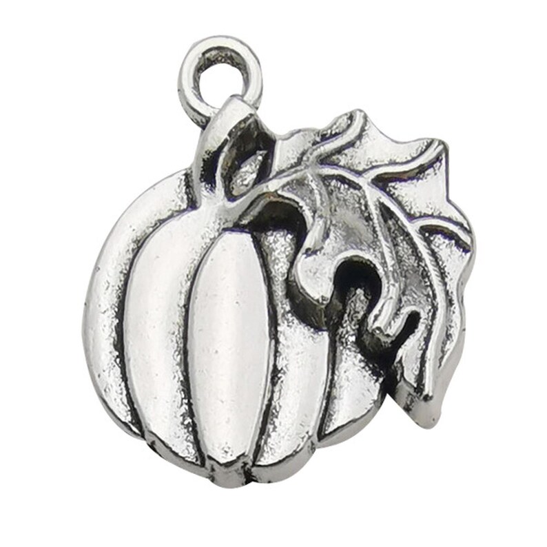 May include: A silver-toned metal charm shaped like a pumpkin with a single leaf attached to the side. The charm features a circular jump ring at the top for attachment, with raised ridges on the pumpkin and detailed veins on the leaf surface.