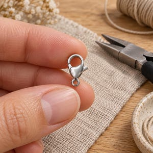 Silver stainless steel lobster clasps. Example of handling the component; tools are not included. 6 x 12mm. Buyer pack: 10 pieces.
