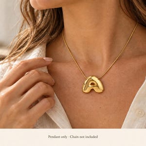 May include: A gold-toned, puffed letter A pendant with a smooth, reflective surface. The pendant features a rounded, three-dimensional shape and a small loop at the top for attachment to a chain. The text below the image states: Pendant only.