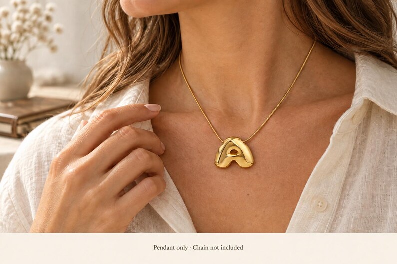 May include: A gold-toned, puffed letter A pendant with a smooth, reflective surface. The pendant features a rounded, three-dimensional shape and a small loop at the top for attachment to a chain. The text below the image states: Pendant only.