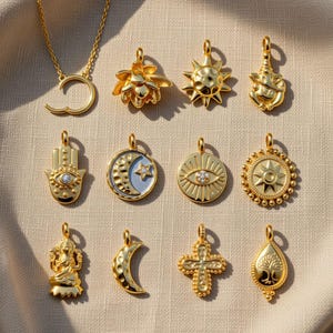 May include: A collection of gold-colored pendants featuring various designs, including a sun, lotus flower, Hamsa hand, moon and star, and an eye. The pendants are displayed on a neutral-colored surface, showcasing their intricate details and reflective surfaces.
