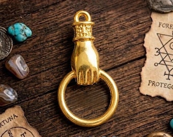May include: A gold-colored charm in the shape of a hand holding a ring. The charm is on a wooden surface with other small objects. The text "X10 PCS" is at the bottom of the image.