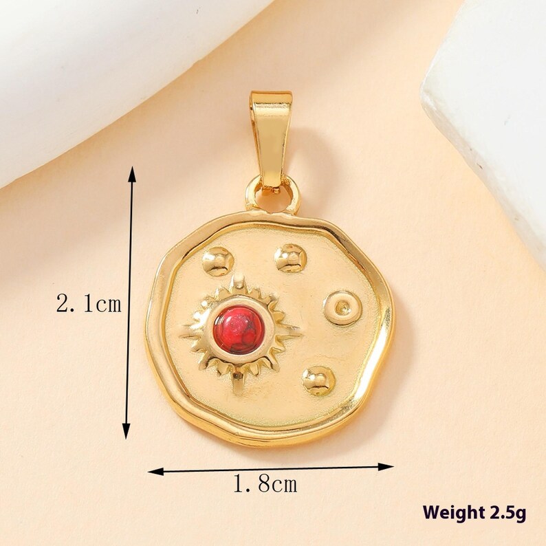 May include: A gold-toned pendant featuring a circular, irregular shape with a central sun motif containing a red stone. The pendant includes small raised dots and measures 2.1 cm by 1.8 cm with a weight of 2.5 grams. It has a top bail for hanging.