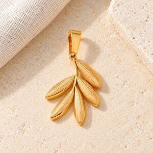 May include: A gold-toned metal pendant shaped like a small branch with five smooth, elongated leaves. The pendant features a polished finish and a sturdy, integrated bail at the top for attachment to a chain or cord, showcasing a botanical design.